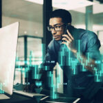 Shot Of A Young Man Using His Cellphone While Working On A Computer In A Modern Office
